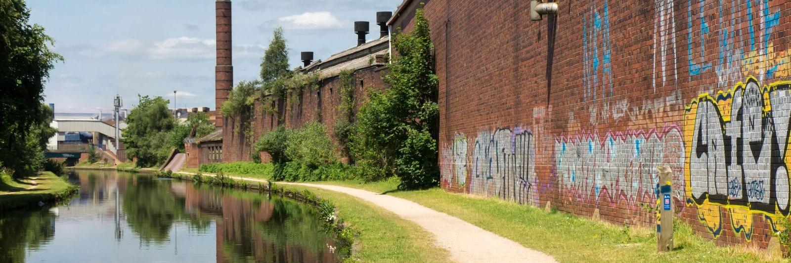 urban canal on still summer day with cream stone towpath and red brick wall with colourful graffiti Photo Nick Thorne Bodian Photography